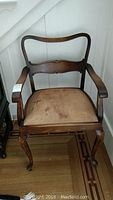 Front view of antique chair showing curved backrest, armrests, and leather upholstered seat