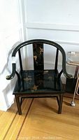 Full view of the black enamel solid wood occasional chair with curved arms and floral design on seat and backrest.