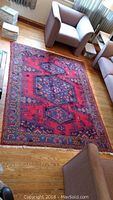 Full view of red Persian rug laid on hardwood floor between armchairs
