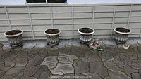 Four composite urn-style planters on patio with two small decorative pots at one end
