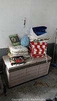 Full view of storage box with cushions and fabric items piled on top.