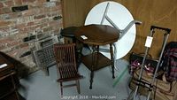 Vintage wooden side table with octagonal top, lower shelf, and turned legs with two wooden folding tables and wooden chair near a brick wall.