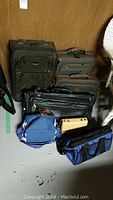Overall view of the collection of bags including suitcases, cooler bags, leather bags, all placed on floor against wood background