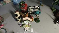 Top-down view of all animal figurines grouped together on floor including metal bird, wooden cat, rooster, cow, sheep and others