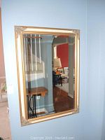Framed beveled wall mirror hanging on blue wall reflecting interior with staircase and furniture.