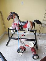 Photo showing Hedstrom bouncy horse on black metal spring frame with painted horse figure, plush horse giddyup stick attached to frame, and vintage tricycle in front