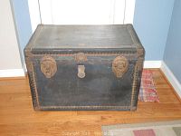 Full frontal image of black rectangular vintage steamer trunk showing top, front, and metal latch details.