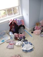 Wide view of all doll clothes spread on carpet, showing checked dresses, rollerblades, and panda doll accessory.