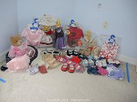 Full view of many Build-A-Bear outfits and accessories including a bear dressed in pink satin and multiple packaged outfits.