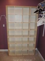 Front view of the entire cubby storage unit showing 25 cubbies arranged in a 5x5 grid against a purple wall.