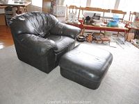 Front angle of dark grey leather armchair and ottoman on carpeted floor with visible wear on leather surfaces.
