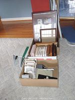 Box and stack of assorted frames in varying sizes and styles on a carpeted floor