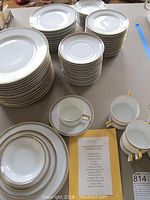 Stacked plates, bowls, cups, and saucers showing gold and black patterned trim with gold rim and handles on cups.