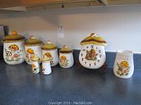 Full view of all eight pieces including six canisters, mushroom clock, and utensil holder with mushroom motifs.