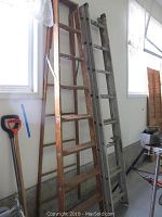 Photo showing two wooden ladders, one step ladder and one extension ladder, positioned side by side indoors near windows, showing wear and signs of use.