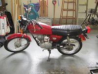 Side profile of motorcycle showing red tank, Honda logo, 125 side cover, center stand