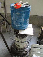 Kerosene heater with blue metal fuel canister on top in unfinished room.