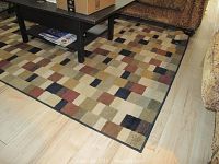 Photo showing the checker pattern and color variety of the rug under a black coffee table and part of furniture to give scale.