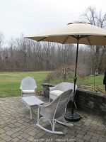 Patio furniture set shown outdoors on stone patio, includes umbrella, loveseat, rocking chairs, and coffee table.