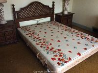Full view of the queen size wooden bed frame with floral pattern mattress on it and nightstands beside.