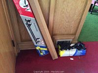 Photo of Thule System 1061 ski rack in box leaning against wood panel wall on red carpet, with another large box next to it and a bundle of hardware accessories on the floor.