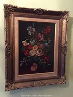 Framed floral oil painting on wall, showcasing overall piece and ornate gold-colored frame.