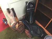 Photo showing several wooden tennis rackets including Dunlop Maxply in press with cover, leather baseball glove, and additional rackets leaning against wall.