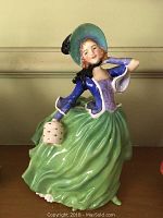 Front view showing detailed facial features, bonnet, blue jacket, green skirt, and muff