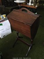 Wooden sewing box on stand, showing front view with lid closed and handle visible