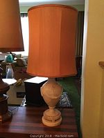 Full view of the stone table lamp with its beige fabric lampshade on a wood surface, showing its height and color.