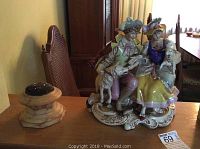 Overall view of the porcelain figurine and pin cushion on a wooden table, showing scale and positioning.