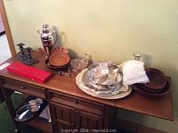 Full view of the lot items displayed on a wooden sideboard with various bowls, trays, silver plate, glass decanter, and boxed carving set visible.