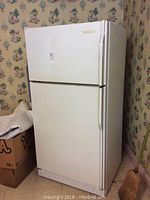 Full view of white KitchenAid refrigerator showing front and left side with visible wear and older wallpaper background.