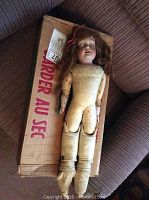 Full body view of antique Morimura Brothers doll lying on a cardboard box, showing intact head and torso but missing feet, arms with discoloration and wear.