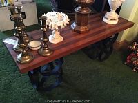 Side and top view of wood table with decorative circular black metal base and various small metal and ceramic decorative items on top.
