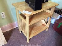 Side view of a light wooden table with vertical slats on the side and two shelves below the tabletop.