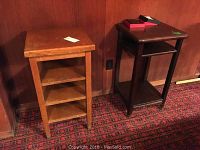Two wood tables side by side, one lighter wood with shelves and one darker wood table with shelves