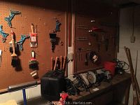 Photo showing pegboard with various tools including paint brushes, clamps, and a black tool case on the bench below.