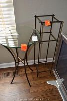 Front and side view of round glass table with metal frame positioned beside high metal stand with glass shelves