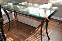 Full view of the rectangular sofa or console table showing the glass top and metal frame with decorative stretcher.