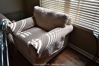 Front-side view of a fabric armchair with armrests and a cushioned seat and backrest near window blinds.
