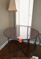 Full view of the round granite top table showing the polished granite surface and metal legs in a cross-braced configuration.