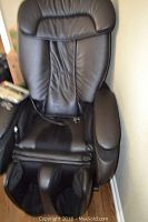 Front view of black massage chair showing headrest, armrests, seat and built-in foot massager.