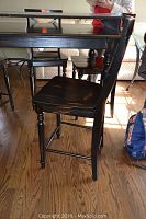 Side profile of one dark finished wooden pub chair showing turned front legs, contoured seat, footrest, and backrest design.