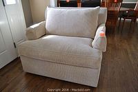 Front view of beige oversized fabric chair with cushion back and armrests on wooden floor.