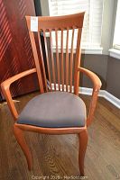 Close-up of an armchair showing curved wooden arms, vertical slat back and dark gray upholstered seat