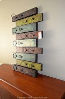 Front view of metal wall art with horizontal metal slats in varying rust red, green, and yellow colors with attached circular metal wine bottle holders.