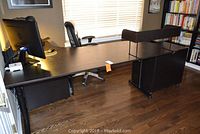 Full view of the wooden black IKEA office desk with the additional raised shelf and part of a black office chair near window.