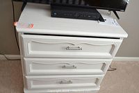 Front view of white chest of drawers with three drawers and silver handles.