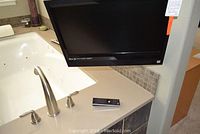 Photo showing the Vizio 22-inch TV mounted beside a sink with remote placed on countertop, demonstrating size and included remote.